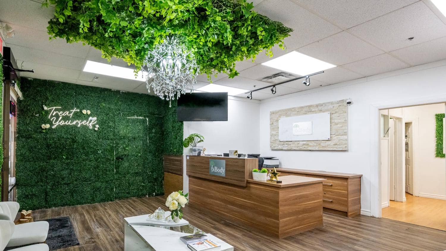 The iBODY reception: a living green wall with a "Treat Yourself" neon sign, a crystal chandelier and the front desk